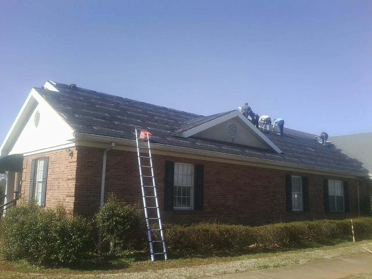 Crew tearing shingles off a brick ranch roof with a ladder set — Emergency Roof Repair work by our crew in Gerlach