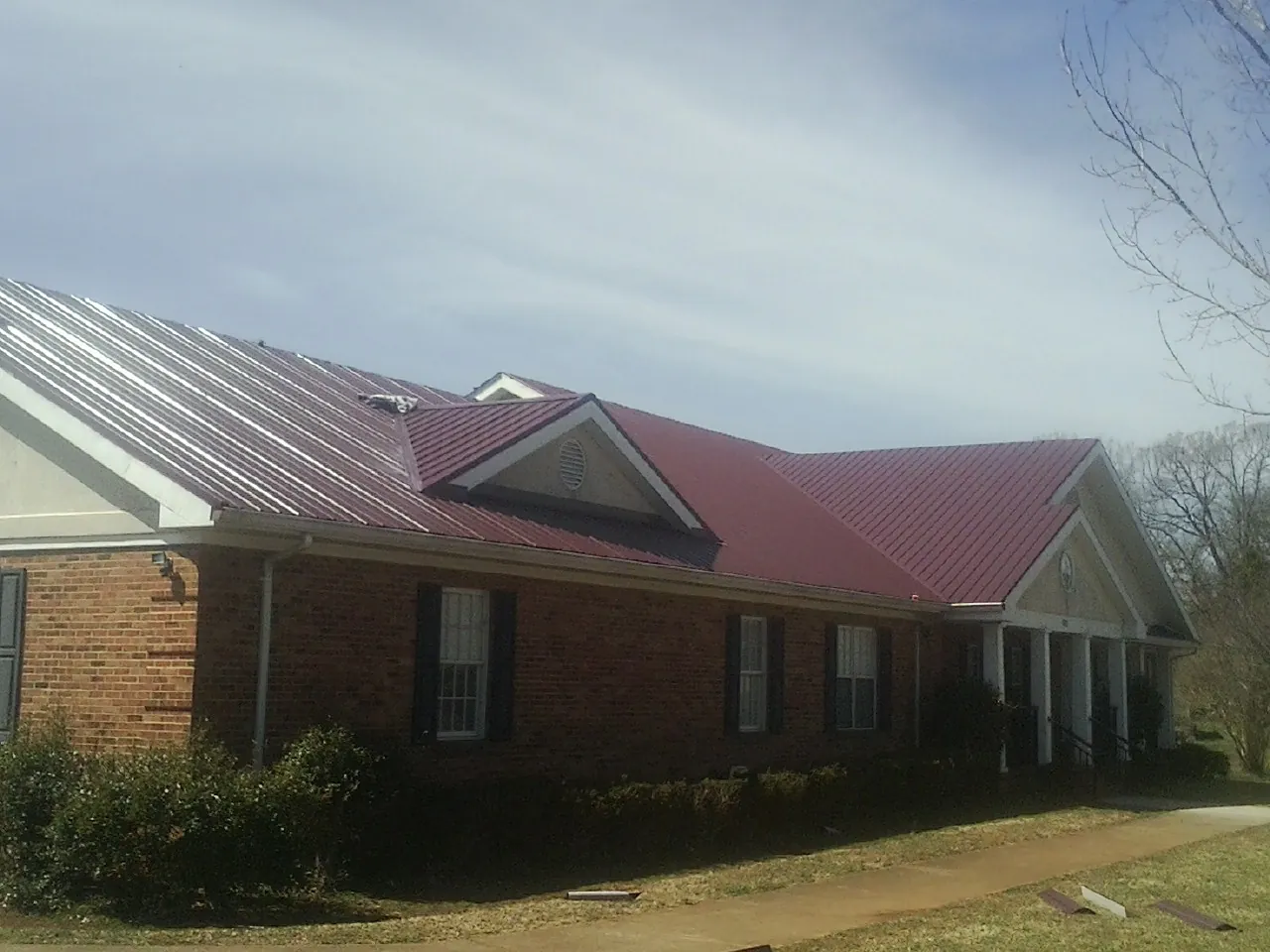 Red metal roof with gabled entries on a long brick building, from a Hail Damage Roof Repair job in Gerlach