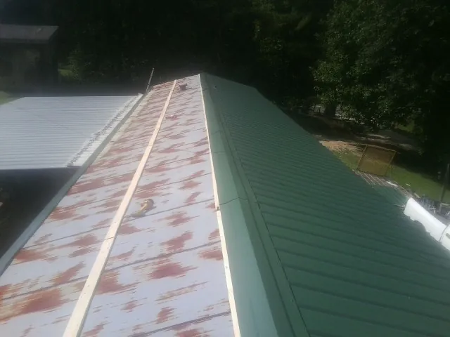 Old rusted panels beside newly installed green metal roofing — Wind Damage Roof Repair by Roofing Brothers in Gerlach