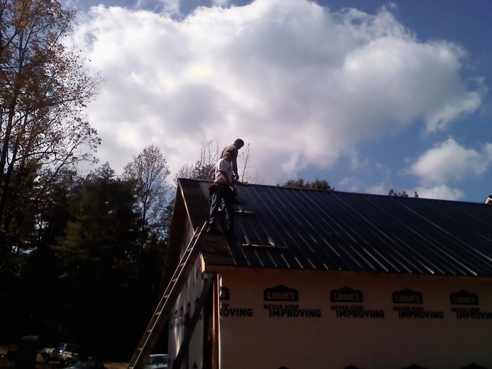 Roofer fastening dark metal panels high against a cloudy sky, from a Roof Inspection job in Gerlach